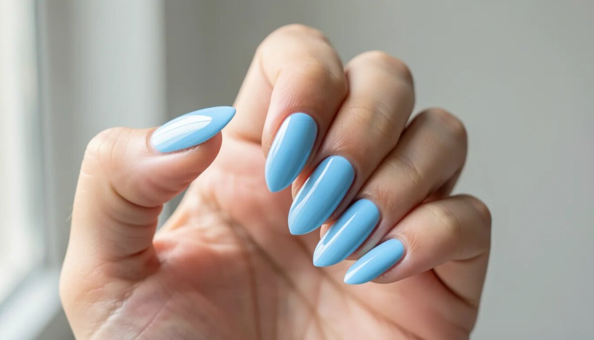 Mão feminina com unhas decoradas em gel azul bebê, acabamento brilhante e cutículas hidratadas.
