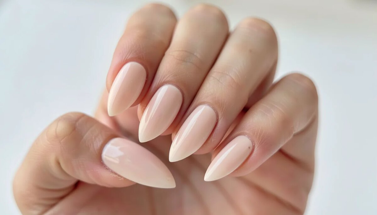 Mão com unhas de fibra de vidro finalizadas, formato amendoado, brilho intenso, fundo claro.