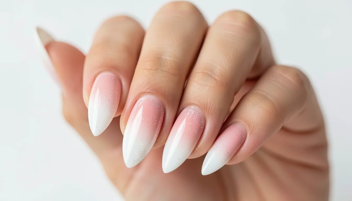 Mão feminina com unhas decoradas em estilo baby boomer com glitter sutil, fundo branco.