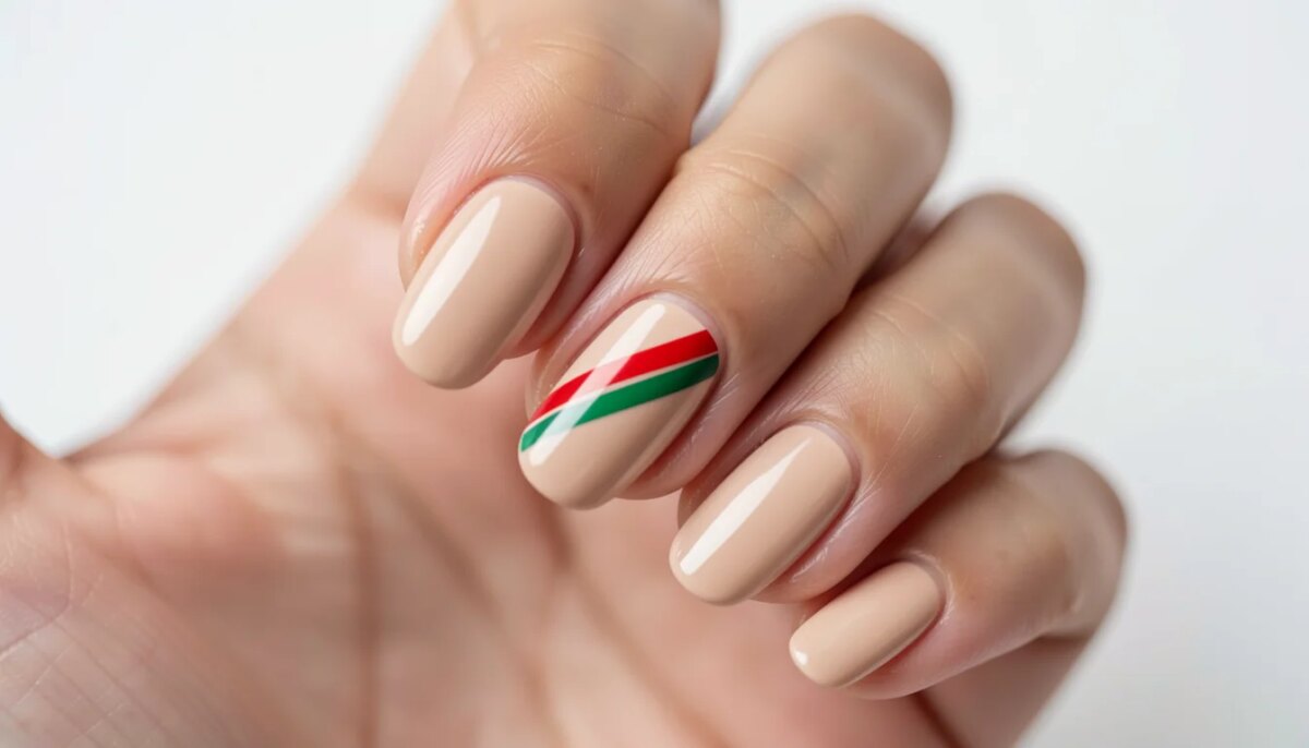 Mão feminina com unha decorada junina simples: bandeirinha vermelha e verde sobre base nude.